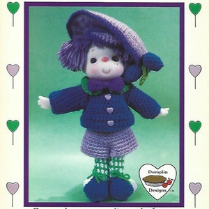May include: A crocheted doll wearing a purple hat, blue jacket, purple pants, and green and white striped socks. The doll has a purple and green flower on its head. The doll is standing on a green background. The text "Plum Preserves" is at the top of the image. The text "Dumplin Designs" is at the bottom of the image.