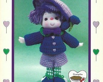 May include: A crocheted doll wearing a purple hat, blue jacket, purple pants, and green and white striped socks. The doll has a purple and green flower on its head. The doll is standing on a green background. The text "Plum Preserves" is at the top of the image. The text "Dumplin Designs" is at the bottom of the image.