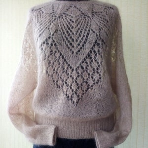 May include: A delicate, light pink knitted sweater with a lacy pattern on the front and long sleeves.