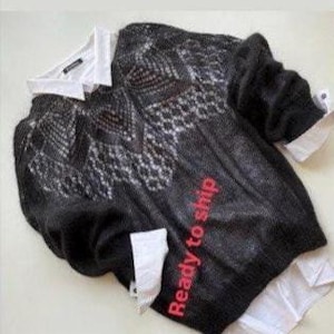 May include: A black sweater with a white and gray patterned design, layered over a white collared shirt. The sleeves of the shirt are visible. The words "Ready to ship" are printed in red on the sweater.