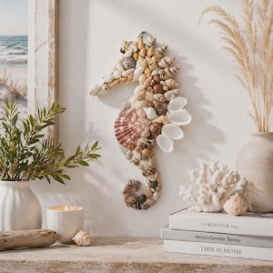 May include: A seahorse wall decoration made from assorted seashells in beige, brown, and white hues. The seahorse has a large, reddish-brown shell in the middle and is mounted on a white wall. Decorative items include a vase with dried grass and a coral sculpture.