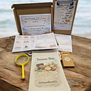 Könnte beinhalten: Ein Küsten-Schnitzeljagd-Set mit einer Schatzbeutel, Lupe und Checkliste. Das Set enthält ein Zertifikat, kreative Challenge-Karten und eine Box. Der Schatzbeutel zeigt eine Strandszene mit Muscheln und einer Schatzkiste.