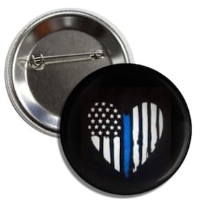 May include: A black button with a white heart-shaped American flag with a blue line down the middle. The button is for sale.