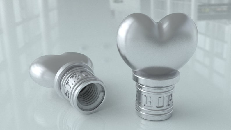May include: Two silver heart-shaped bottle stoppers with threaded bases. The stoppers are made of metal and have a shiny finish.
