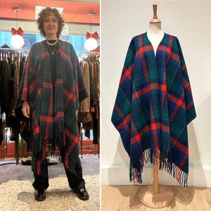 Può includere: Un poncho a quadri blu navy, verde e rosso, con orlo a frange. Il capo è mostrato su un manichino e indossato da una persona. Il motivo a quadri è un design classico, adatto per l'autunno e l'inverno.