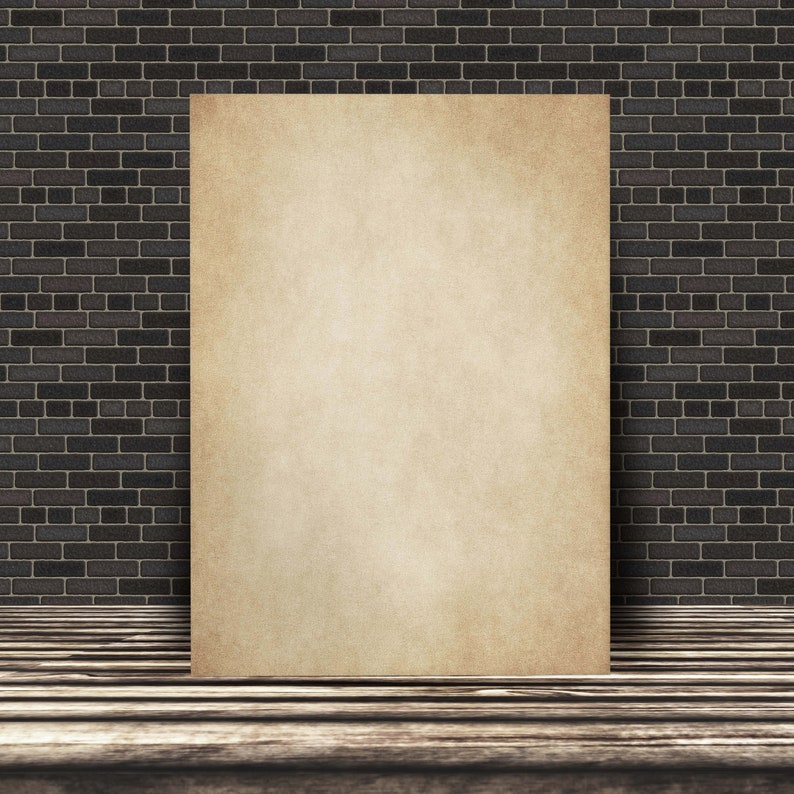 May include: A blank, aged, cream-colored paper poster is leaning against a dark brick wall. The poster is in front of a wooden floor.