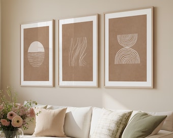 Könnte beinhalten: Drei gerahmte abstrakte Kunstdrucke mit weißen Passepartouts. Die Drucke zeigen minimalistische Designs in Weiß auf braunem Hintergrund. Die Designs umfassen eine Sonne und Wasser, fließende Linien und ein Halbkreis-Design. Die Drucke werden über einem weißen Sofa angezeigt.