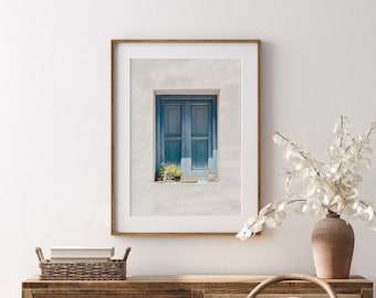 Peut inclure: Une photographie encadrée d'une fenêtre en bois bleu avec des moulures blanches et des plantes en pot sur un mur blanc. La fenêtre est fermée et comporte deux vitres. La photo est dans un cadre en bois simple.
