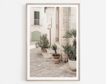 May include: A photograph of a narrow, white-walled alleyway in a European city. The alleyway is lined with potted plants and features a green door and a stone staircase. The image is taken from a low angle, giving the viewer a sense of perspective.