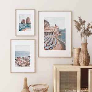 May include: Three framed photographs of Italian coastal scenes. The top photo shows a boat sailing towards a rocky island. The middle photo shows a beach with blue and white striped umbrellas and a town in the background. The bottom photo shows a rocky beach with blue and white striped lounge chairs.