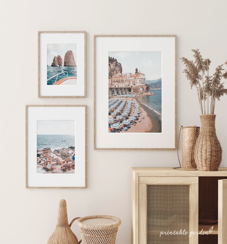 May include: Three framed photographs of Italian coastal scenes. The top photo shows a boat sailing towards a rocky island. The middle photo shows a beach with blue and white striped umbrellas and a town in the background. The bottom photo shows a rocky beach with blue and white striped lounge chairs.