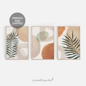 以下が含まれることがあります： ベージュ、ブラウン、グリーンのニュートラルなカラーパレットを使用した、抽象的なアートプリント3枚セット。プリントには抽象的な形と、各プリントに1枚のヤシの葉が描かれています。