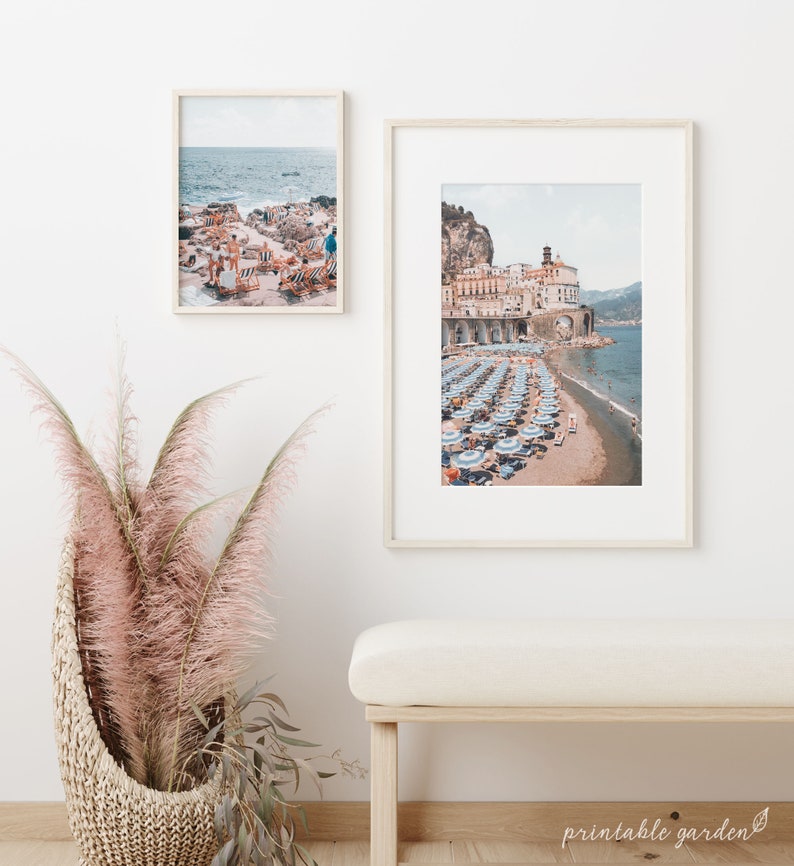 May include: Two framed photographs of a beach scene with blue and white striped umbrellas and lounge chairs. The top photo shows a view of the ocean with a rocky shoreline. The bottom photo shows a view of a town with buildings and a beach.
