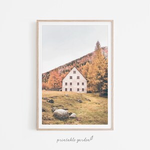 May include: A white house with many windows sits on a grassy hillside surrounded by trees with fall foliage. The house has a triangular roof and is surrounded by a field of green grass.