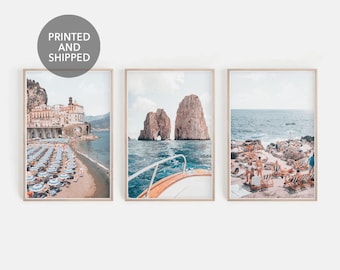 May include: Set of three framed prints featuring coastal scenes. One print shows a beach with umbrellas, another a boat near rock formations, and the third a beach with lounge chairs. The prints have a light, airy aesthetic, perfect for home decor.