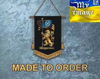 Puede incluir: Una pancarta negra con ribetes y borlas doradas cuelga de una cuerda. La pancarta presenta un león dorado sosteniendo una bandera con una W azul y dorada. El texto "Wagnerman" está impreso en dorado en la parte inferior de la pancarta. La pancarta se hace por encargo.