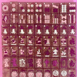 May include: A set of rectangular mahjong tiles arranged in a grid, crafted from translucent resin with embedded pink glitter. Each tile features engraved symbols, numbers, and characters in shades of pink and white, representing standard game pieces.