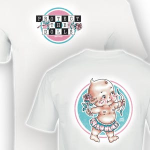 Puede incluir: Camisetas blancas con un diseño gráfico. Una camiseta presenta el texto "PROTECT THE DOLLS" en un diseño negro, rosa y azul. La otra camiseta tiene un cupido de dibujos animados con arco y flecha, sosteniendo una rosa, dentro de un círculo rosa y azul.