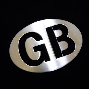 May include: A silver oval-shaped car emblem with the letters "GB" in black.