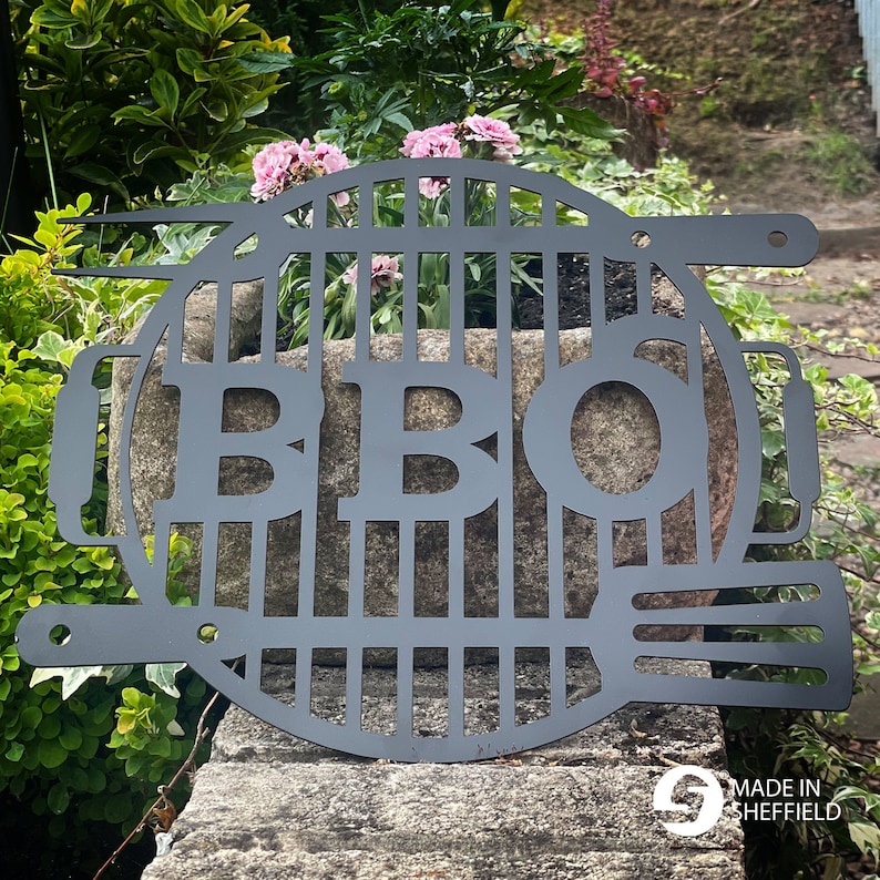 May include: Black metal BBQ grill sign with the letters "BBQ" cut out. The sign is in the shape of a grill grate with a handle on the side. The sign is made in Sheffield.