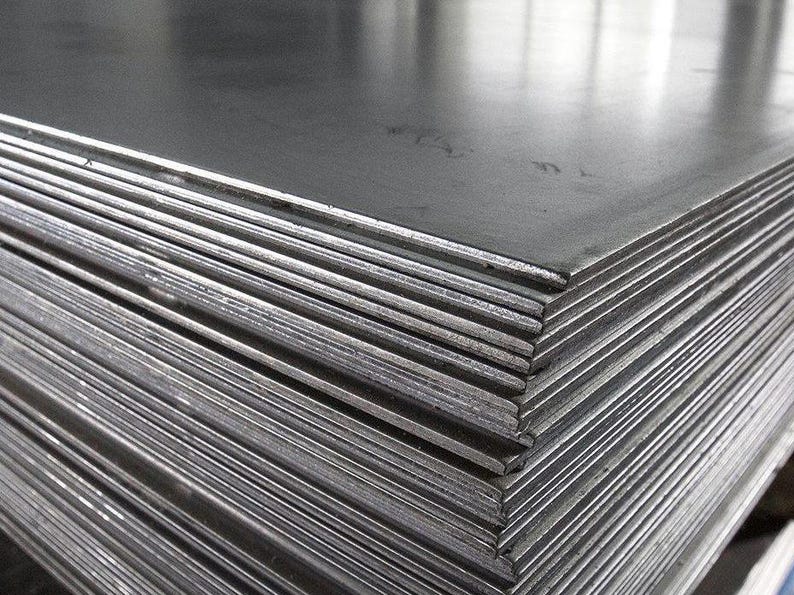 May include: A stack of metal sheets, likely steel, with a smooth, reflective surface. The sheets are stacked neatly, creating a pattern of parallel lines.
