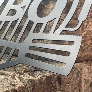 May include: Black metal BBQ grill with a decorative design. The grill is made of metal and has a black finish. The grill is designed to be used for outdoor cooking.