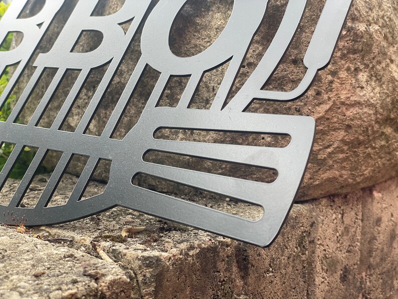 May include: Black metal BBQ grill with a decorative design. The grill is made of metal and has a black finish. The grill is designed to be used for outdoor cooking.