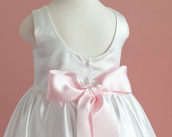 May include: White satin dress with a pink satin bow in the back. The dress has a scoop neckline and sleeveless design.