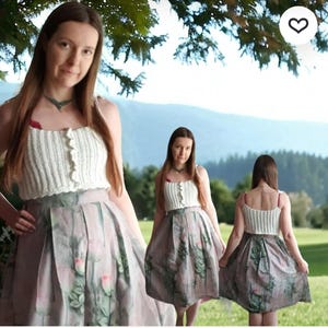 Puede incluir: Un top blanco de ganchillo con un borde festoneado y una falda con estampado floral. La falda es de color rosa suave con acentos florales verdes y rojos. El atuendo se usa al aire libre con un fondo de monta&ntilde;a.