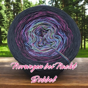 Könnte beinhalten: Eine Garnrolle in den Farben Schwarz, Blau, Grün und Pink. Das Garn ist zu einer Kugel gewickelt und das Etikett lautet "Norwegen bei Nacht Bobbel".