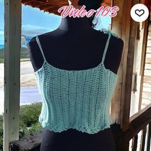 Puede incluir: Top de ganchillo azul claro con tirantes finos. El top se muestra en un maniqu&iacute; negro. El texto "Video 103" es visible en la esquina superior izquierda. El top tiene un borde festoneado.