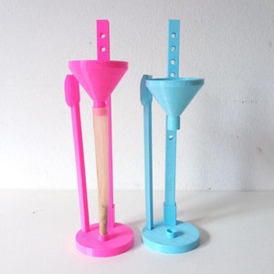 Puede incluir: Dos dispositivos de enrollado de conos impresos en 3D, uno rosa y otro azul. Cada dispositivo tiene un embudo, un soporte y un cono para enrollar.