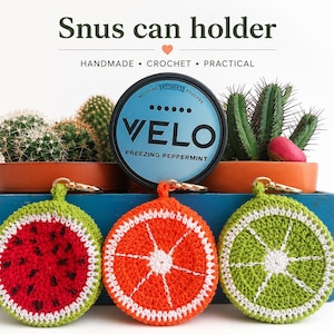 Puede incluir: Soportes de ganchillo para latas de snus con forma de rodajas de fruta: sandía, naranja y lima. Cada soporte tiene un cierre de llavero dorado. La imagen también muestra una lata de bolsitas de nicotina Velo y cactus en macetas.