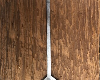 May include: A silver metal arrow pointing upwards, mounted on a brown wooden surface.