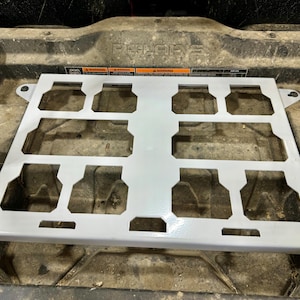 May include: A light gray metal rack with multiple rectangular cutouts, designed for use in a vehicle. The rack has a grid-like structure with a series of evenly spaced openings. The word "POLARIS" is visible in the background.
