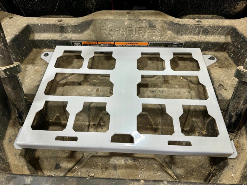 May include: A light gray metal rack with multiple rectangular cutouts, designed for use in a vehicle. The rack has a grid-like structure with a series of evenly spaced openings. The word "POLARIS" is visible in the background.