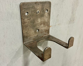 May include: A rustic metal wall mount with a single hook and a curved shelf. The mount has a weathered, aged finish and is designed to hold a variety of items.