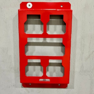 May include: A red metal wall-mounted storage rack with six rectangular cutouts. The rack has a small white knob on the top.