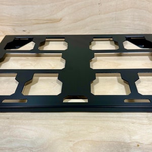 May include: Black metal rack with nine cut-out spaces for holding items. The rack is on a wooden surface.