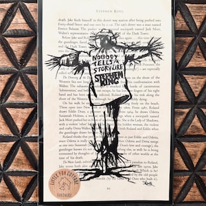 Peut inclure: Une illustration en noir et blanc d'un épouvantail avec le texte "Nobody tells a story like Stephen King" imprimé sur l'image. L'image est imprimée sur une page d'un livre.