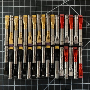 Op de afbeelding: Een verzameling van 24 metalen pijpen met verschillende gekleurde dopjes. De pijpen zijn in rijen gerangschikt en zijn allemaal even groot. De dopjes zijn geel, paars en rood.