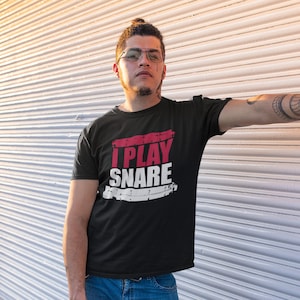 Könnte beinhalten: Ein schwarzes T-Shirt mit einer roten und weißen Grafik, auf der "I Play Snare" steht.