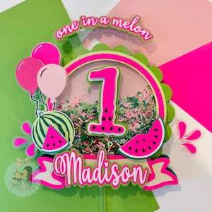 May include: A watermelon-themed birthday cake topper with the number 1 in bright pink. The topper includes a watermelon slice, balloons, and the name "Madison". The phrase "one in a melon" is also included.