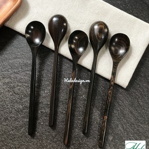 May include: Five wooden spoons with dark brown and black wood grain patterns. The spoons are arranged in a row on a white linen cloth. The spoons are all the same size and shape.