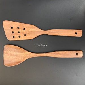Puede incluir: Dos utensilios de cocina de madera, una espátula ranurada y una espátula sólida, ambas con mangos de madera marrón.