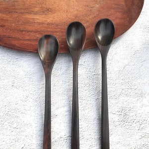 May include: Three wooden spoons of varying sizes, all with a dark brown finish. The spoons are arranged in a row on a white surface.