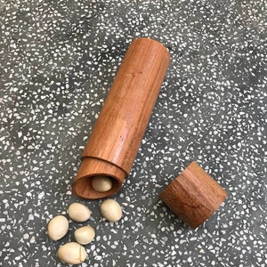 May include: A wooden container with a lid, open to reveal several round, white seeds. The container is made of light brown wood and has a smooth finish.