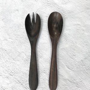 May include: A set of two wooden serving utensils, a spoon and a fork, with dark brown wood grain. The utensils are on a white background.