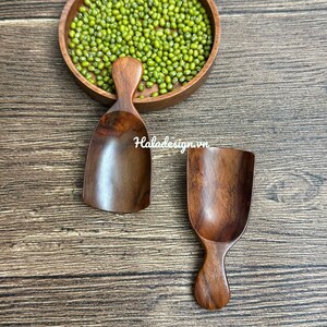 May include: Two wooden scoops and a round wooden bowl filled with green mung beans. The scoops are made of dark wood and have a smooth, polished finish. The bowl is also made of wood and has a natural, rustic look. The text "Haladesign.vn" is visible.
