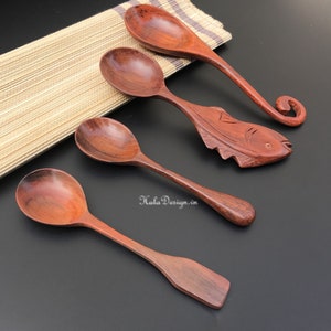 May include: Four wooden spoons of varying sizes, with one spoon carved in the shape of a fish. The spoons are arranged on a brown woven mat and a black surface. The spoons are a reddish-brown colour.